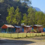 Cottages seen across the lawn at Himalayan Ganga Retreat, trees and forested hills behind, Rishikesh