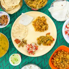 Traditional pahadi thali with dal ki pakodi, roti, til chutney, kafli and a brass glass of chai