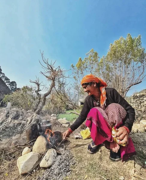 Pahadi woman in traditional attire tending an open wood fire in the Uttarakhand hills