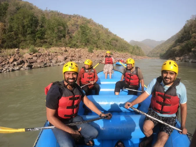 Group river rafting on the Ganga in Rishikesh, paddling a blue raft through Grade II–III rapids