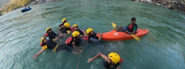 Safety kayaker holding a tow line beside swimmers during a Rishikesh river rafting trip on the Ganga