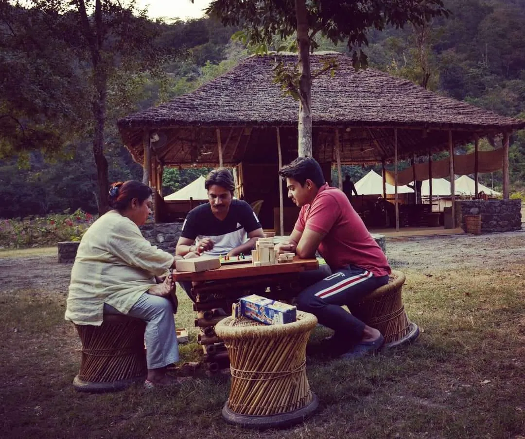 A family playing a board game at a bamboo table by a forest lounge