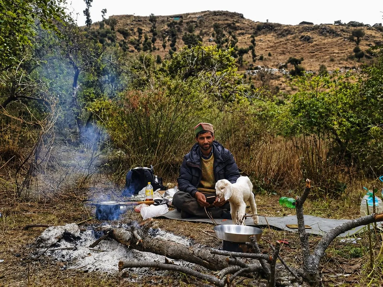 A pahadi shepherd resting by a wood fire with a goat kid in the Uttarakhand hills