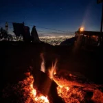 The bonfire burning at night at Camp George Everest, with the lights of the Doon Valley below