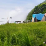 Tents on the grass ridge at Camp George Everest, Mussoorie, with cloud rolling over the hillside behind