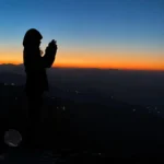 A camper watching dawn from the ridge at George Everest, valley lights still on below