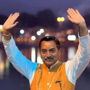 Arms raised during the evening Ganga Aarti at Shatrughan Ghat, Rishikesh, ghat lights blurred behind