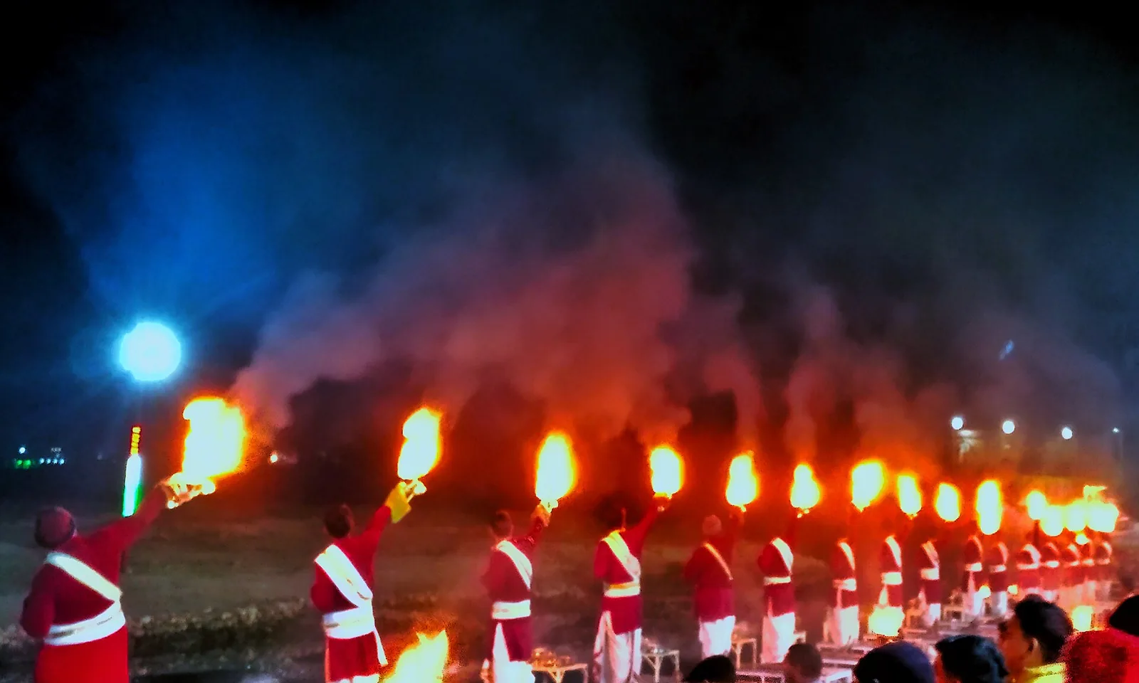 Priests in red robes holding rows of burning aarti lamps above the Ganga at Triveni Ghat, Rishikesh
