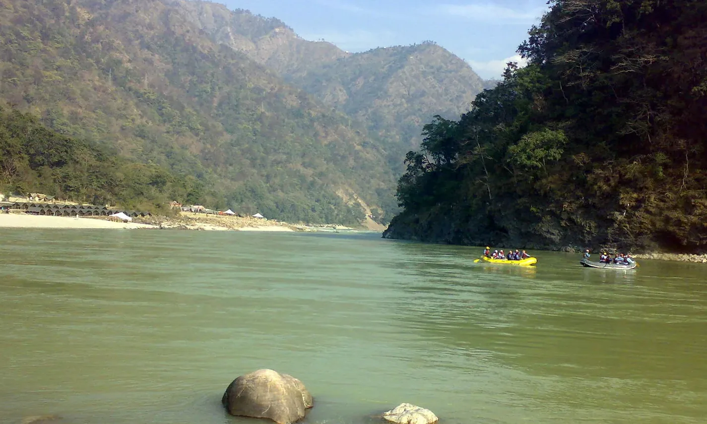 The Ganga running green through a forested gorge upstream of Rishikesh, rafts on the far bank