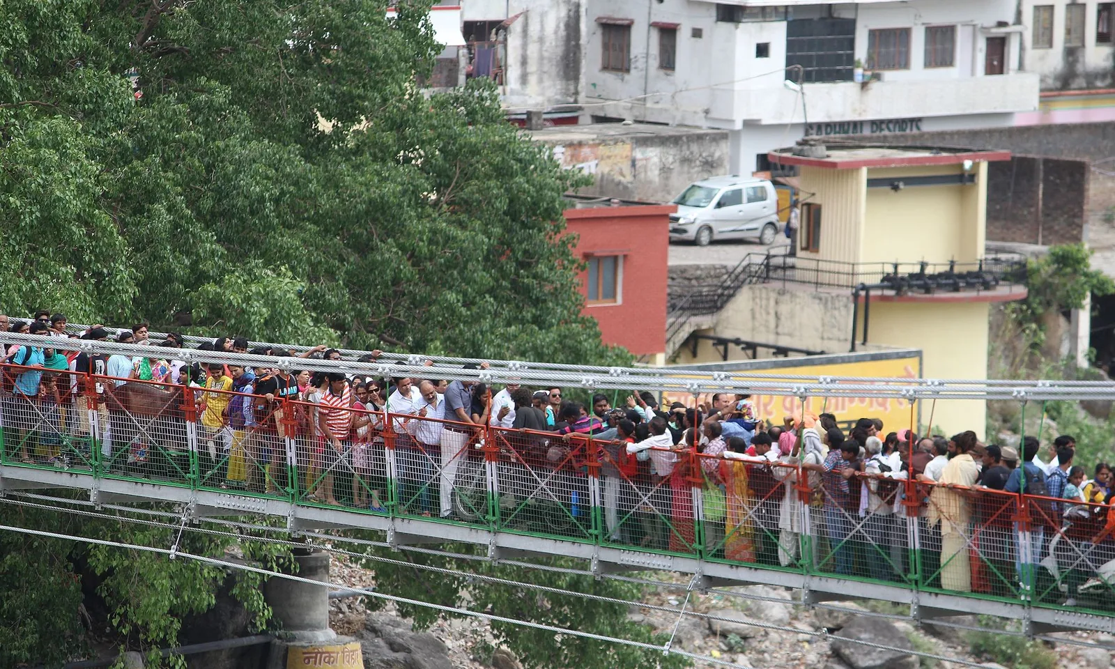 Crowds packed shoulder to shoulder on a pedestrian suspension bridge over the Ganga at Rishikesh