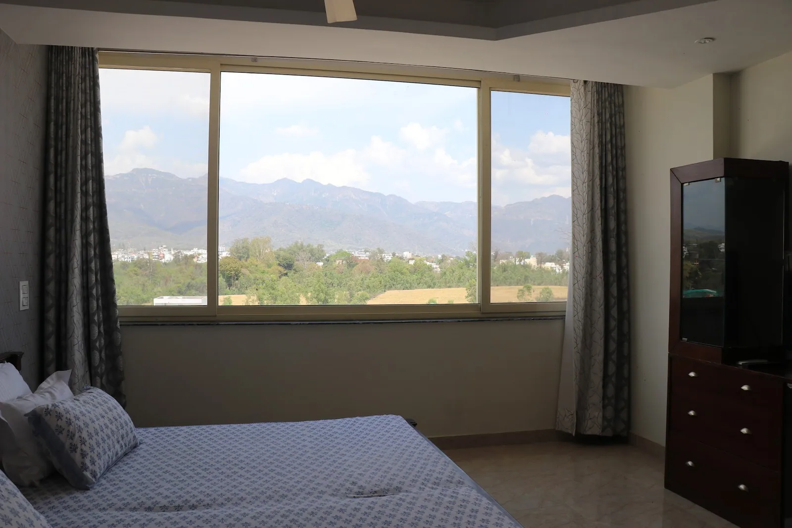 Bed by the window with the hills beyond at Little Sparrow Homestay, Rishikesh