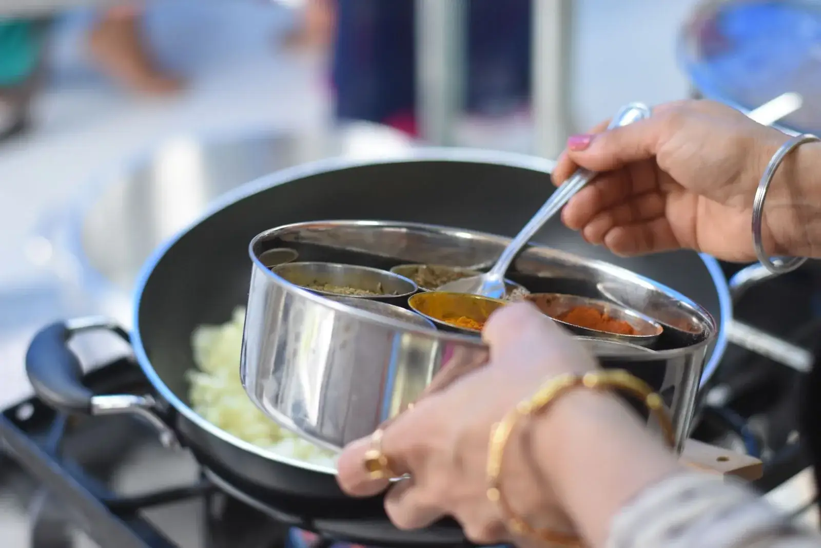 Hands preparing Indian spices in a pan during a cooking class
