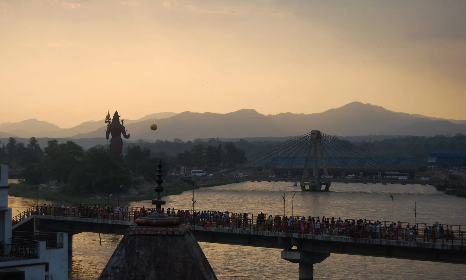 Evening over the Ganga at Rishikesh, crowds crossing the bridge and the Shiva statue on the bank